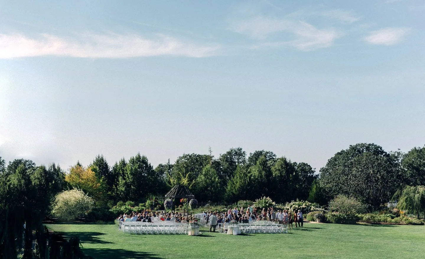 An open green lawn with trees and a few tables in the distance