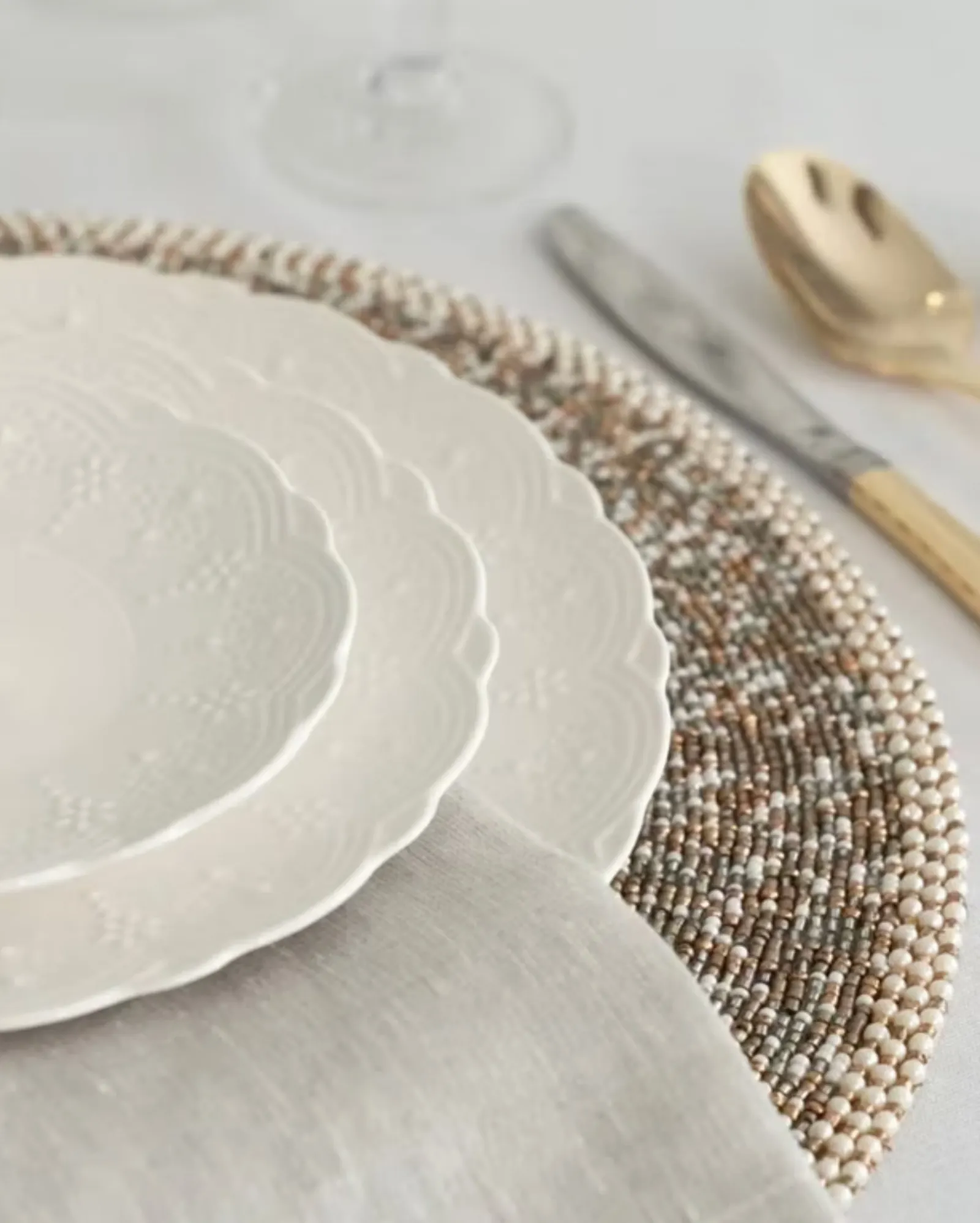 A close-up of layered plates on a beaded charger beside gold flatware