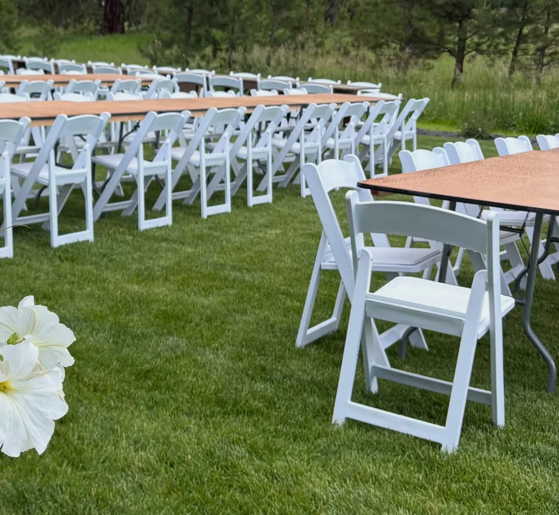 A wood table and white folding chair on a green lawn