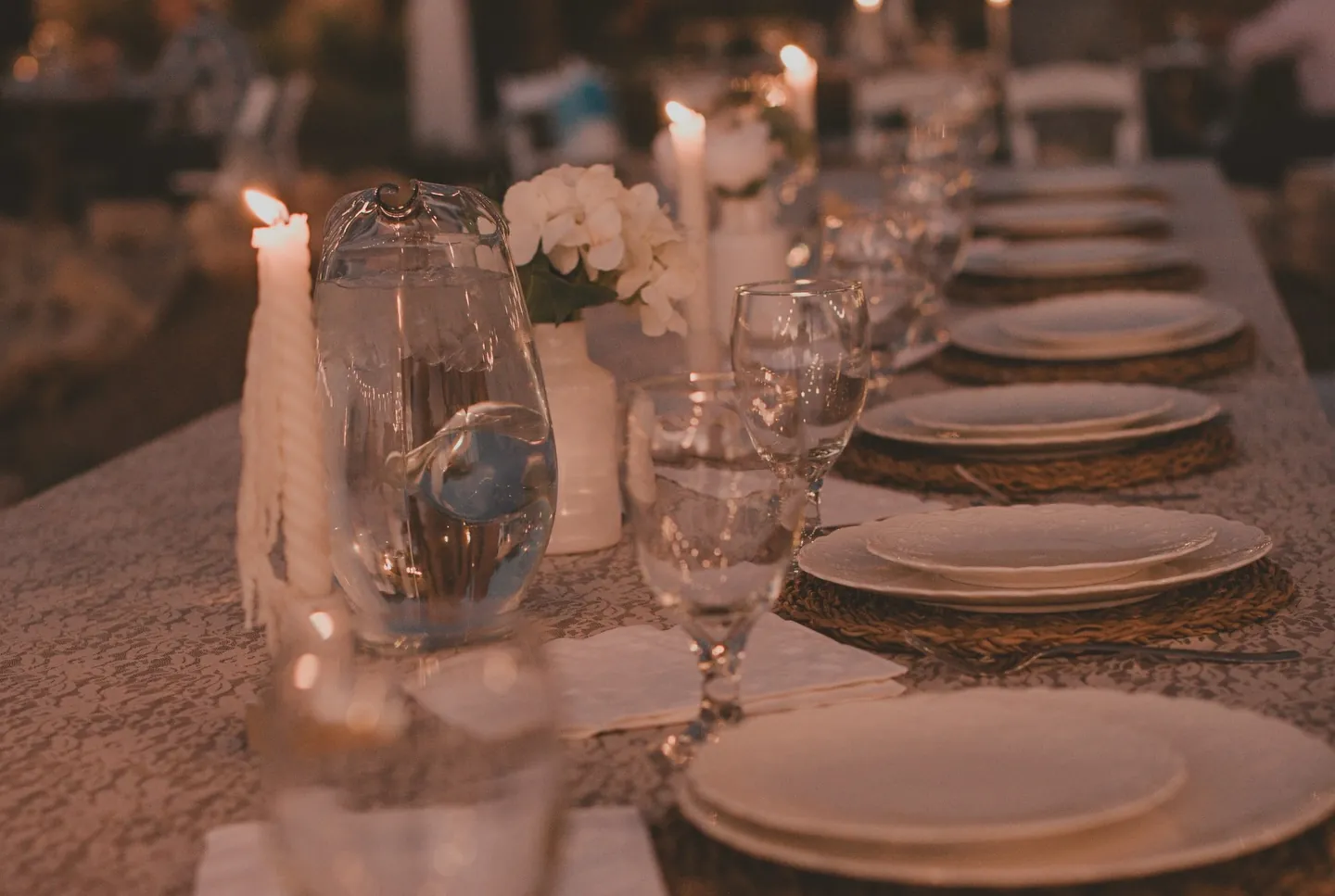 Candles, glassware and layered plates on a long table at night