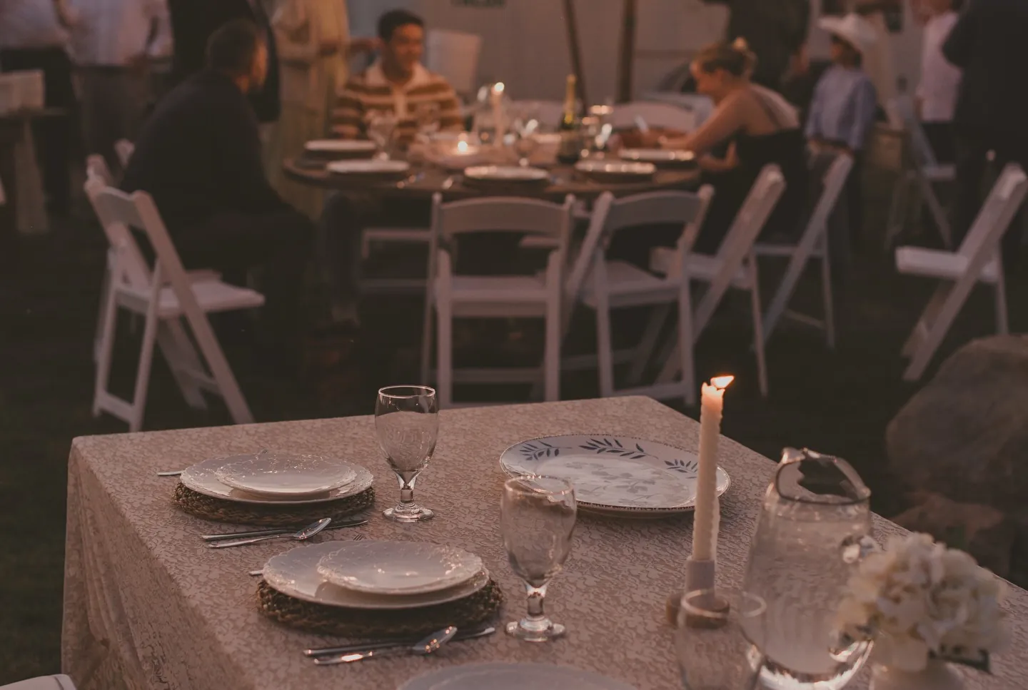 Guests seated at a candlelit round table with glasses and layered plates