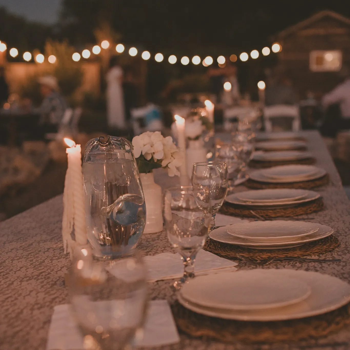 A candlelit table at night under strings of round lights