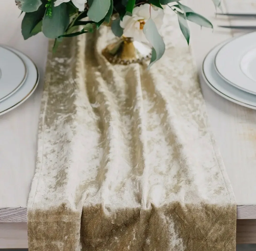 A champagne table runner with greenery, white flowers and plates